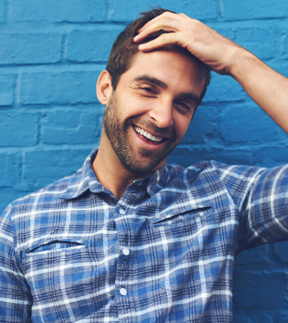 young male smiling against blue brick wall